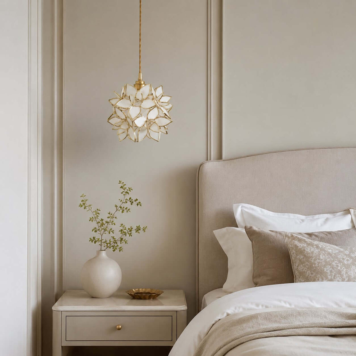 Small white petal Clérachic pendant hanging high above a cream headboard and a bedside table with a vase of green stems.
