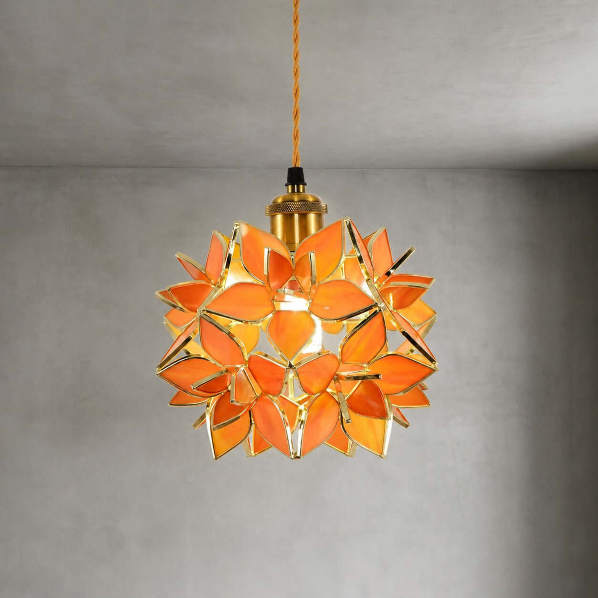 Close view of the orange glass petals and brass socket on this Clérachic pendant, lit and hung against a grey wall.
