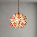 Close view of this Clérachic pendant with pink glass petals edged in gold, lit on a braided cord against a grey wall.