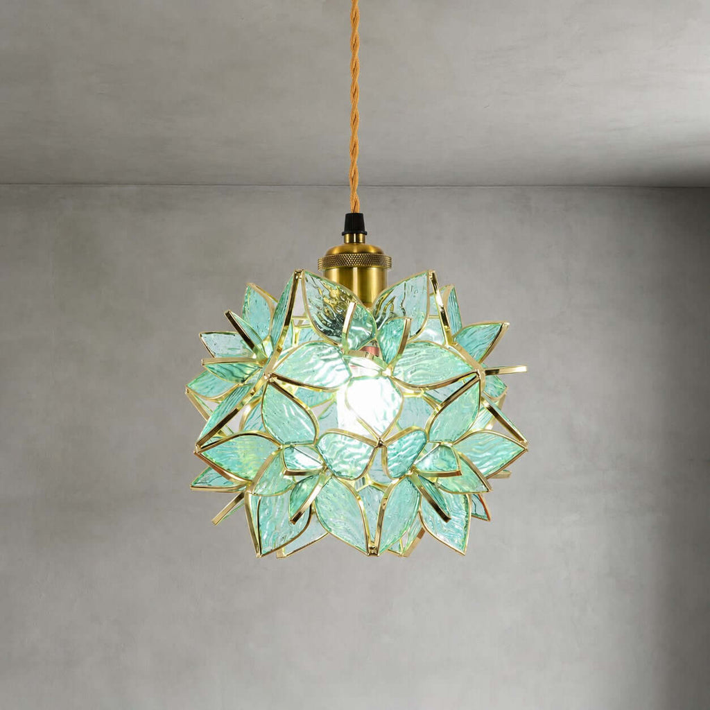 Close view of the green textured glass petals and brass socket on this Clérachic pendant, lit against a grey wall.