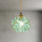 Close view of the green textured glass petals and brass socket on this Clérachic pendant, lit against a grey wall.