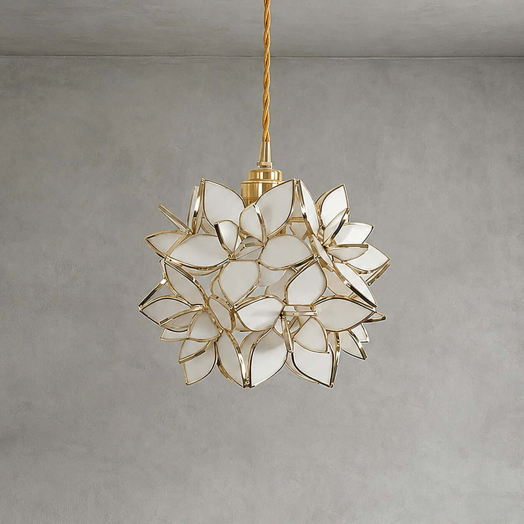 A Clérachic pendant with white glass petals edged in gold, shown unlit on a braided cord against a grey wall.