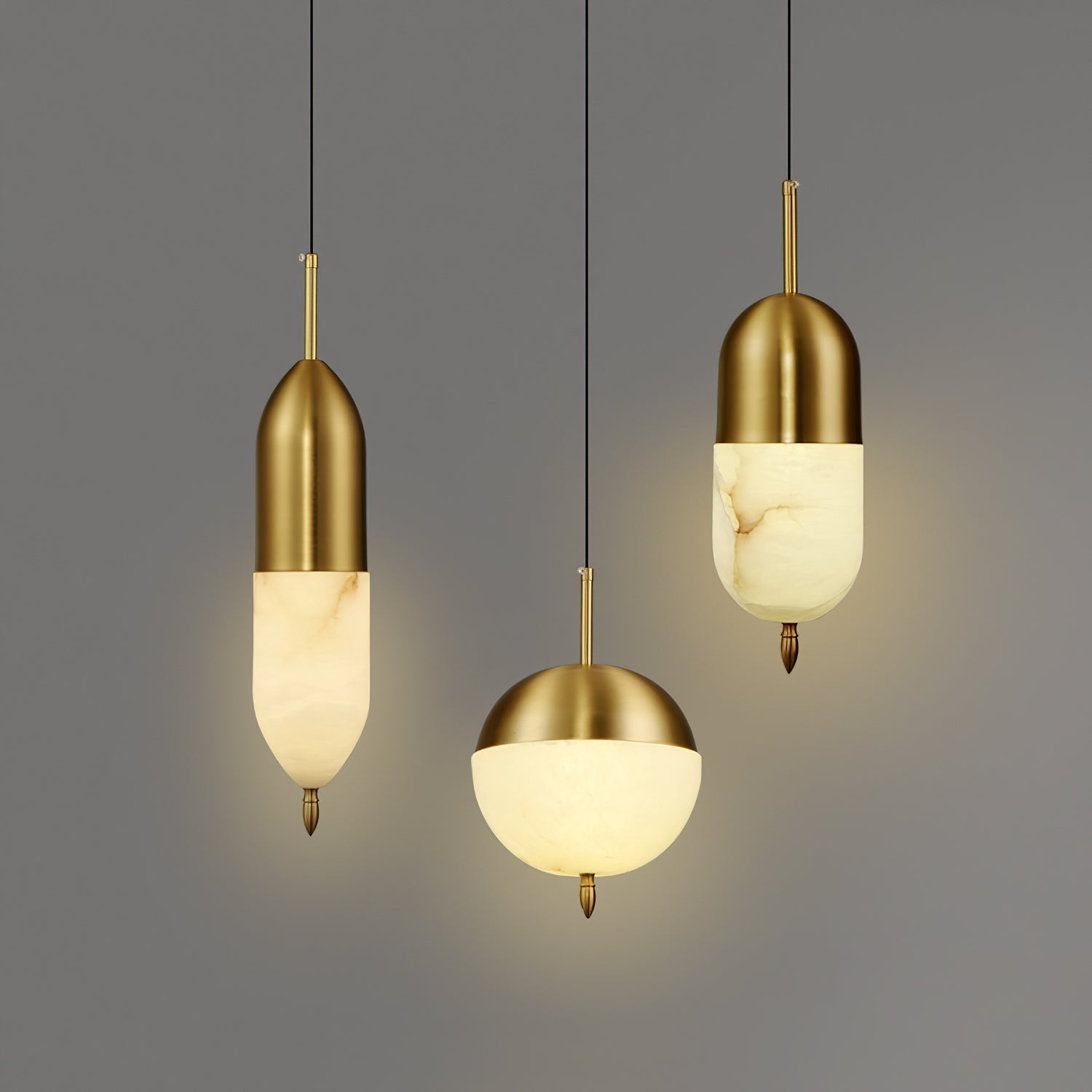 Clérachic Brass Pendant Light in three Spanish alabaster shapes: tall capsule, globe, and rounded pill, glowing on grey.