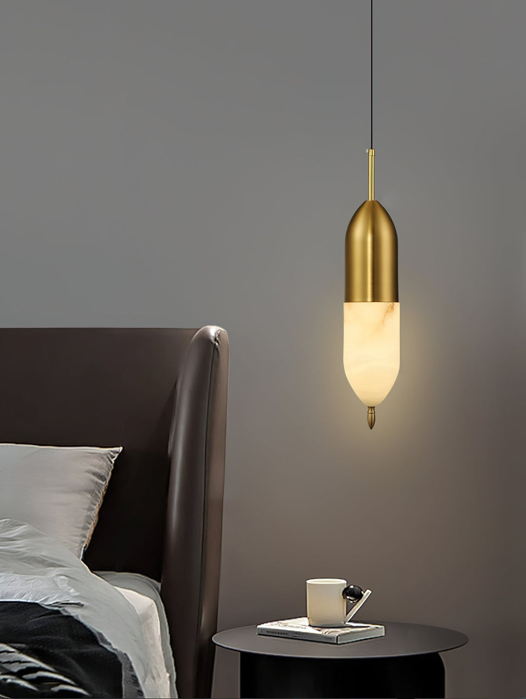 Clérachic Brass Pendant Light beside a leather headboard, glowing over a dark round table with a mug and book.