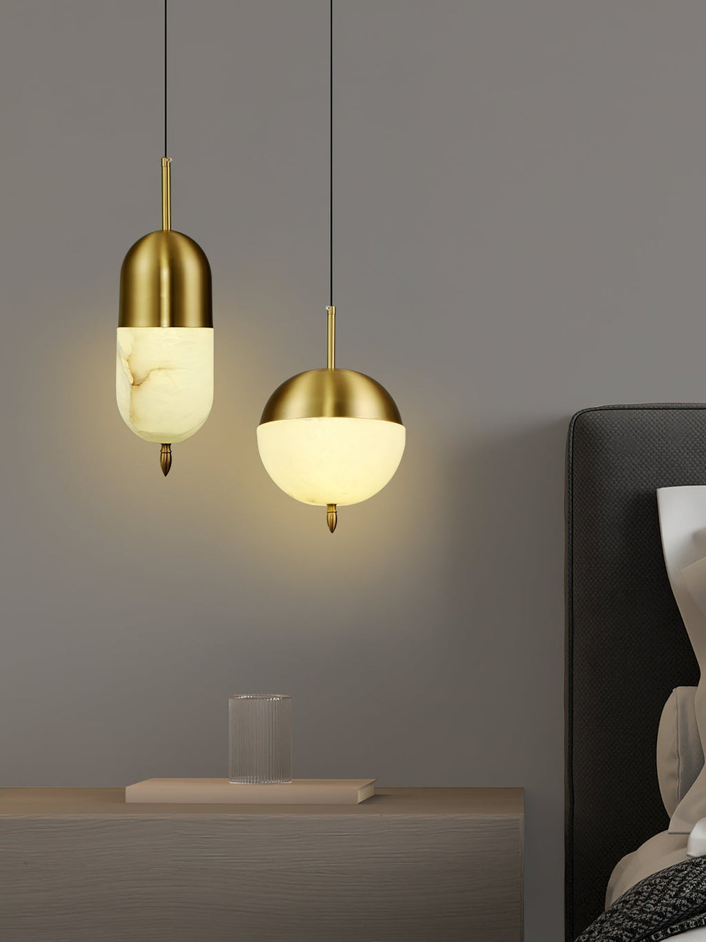 Two Clérachic Brass Pendant Lights — tall capsule and globe — over a wood nightstand with a book and fluted glass.