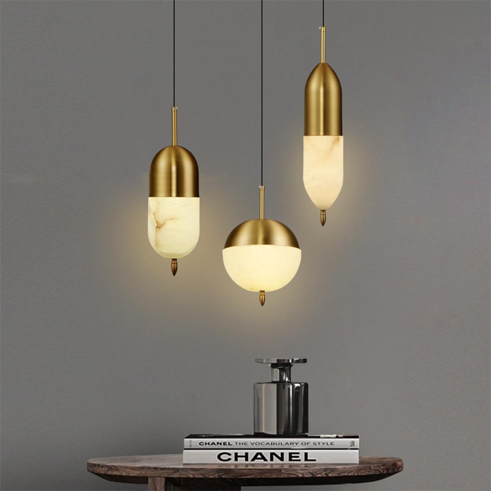 Staggered Clérachic Brass Pendant Lights in capsule, globe, and slim forms above a wood table and stacked books.