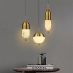 Staggered Clérachic Brass Pendant Lights in capsule, globe, and slim forms above a wood table and stacked books.
