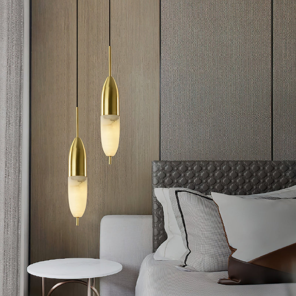 Two Clérachic Brass Pendant Lights over a marble side table beside a hex-quilted grey headboard and wood wall.
