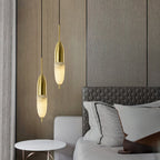 Two Clérachic Brass Pendant Lights over a marble side table beside a hex-quilted grey headboard and wood wall.