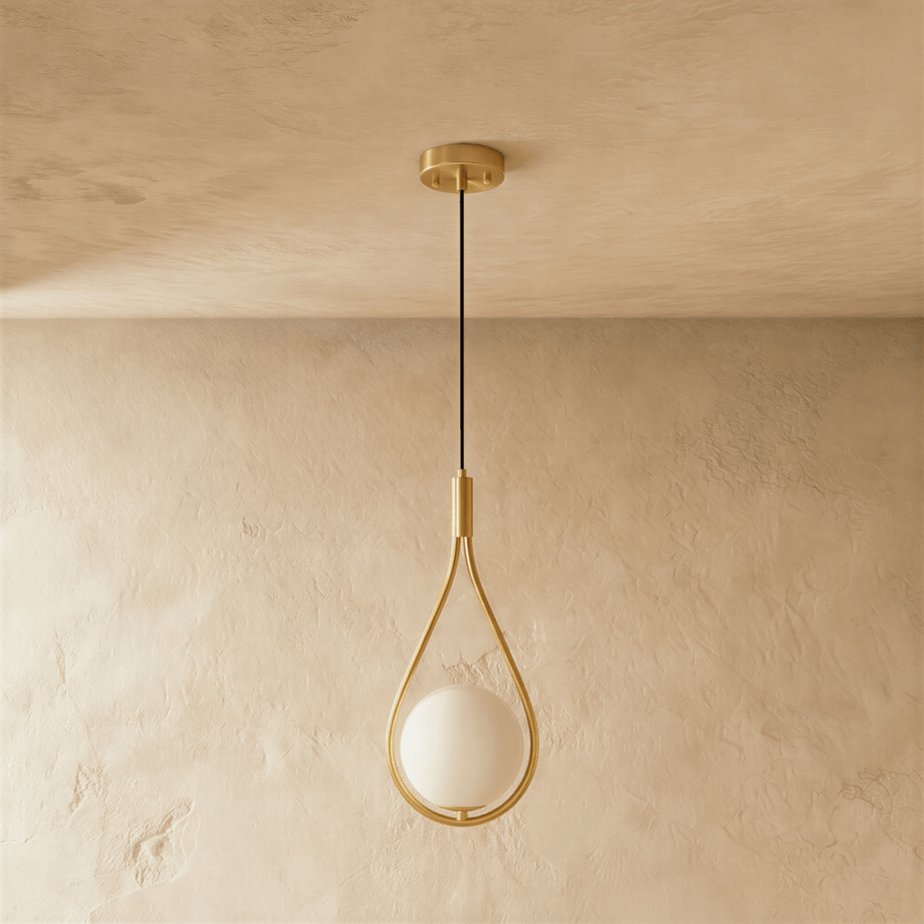 Clérachic teardrop pendant in brushed brass with an opal white globe, switched off, against a soft plaster wall and ceiling.