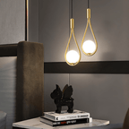 Pair of Clérachic brass teardrop pendants with opal globes glowing over a marble bedside table, an ornament and books.