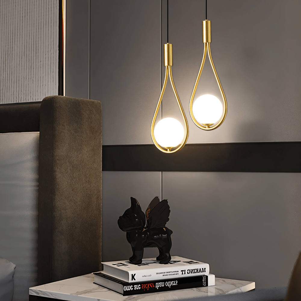 Pair of Clérachic brass teardrop pendants with opal globes glowing over a marble bedside table, an ornament and books.