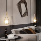 Two Clérachic brass teardrop pendants with glowing opal globes hung at different heights beside a grey sofa and marble side table.