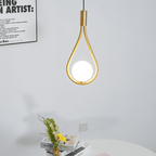 Clérachic brass teardrop pendant with an opal globe hanging against a pale wall above a round table with books and flowers.