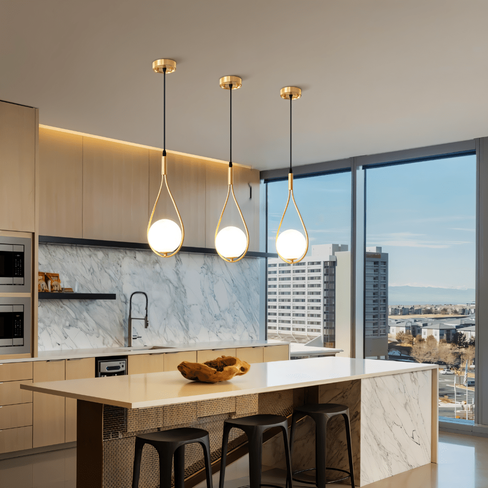 Row of three Clérachic brass teardrop pendants with opal globes over a marble kitchen island with black stools and a city view.