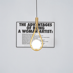Clérachic brass teardrop pendant with a lit opal globe hanging in front of a framed black and white typographic poster.