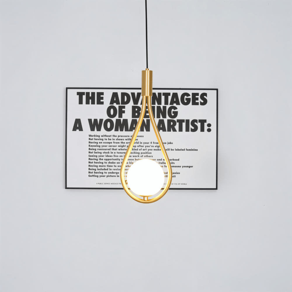 Clérachic brass teardrop pendant with a lit opal globe hanging in front of a framed black and white typographic poster.