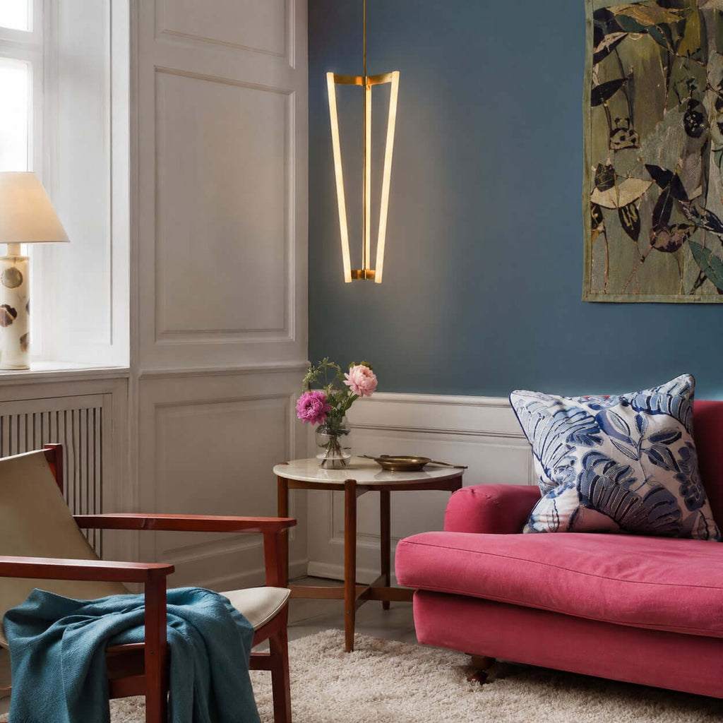 Against a deep blue wall above a side table and a pink sofa, this Clérachic pendant shows its slim lit tubes and brass top bracket.