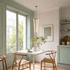Next to a sage-green window frame and a white table, this Clérachic pendant glows with three slim tubes on a brass rod.