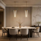 A pair of Clérachic pendants hang side by side above a long oval dining table, in front of a fluted wall and marble panel.