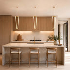 Three Clérachic pendants hang in a line above a stone kitchen island with oak cabinets and three wooden stools beneath.