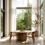 Seen against tall glass doors and sheer curtains, this Clérachic pendant hangs above a round wooden table and curved chairs.