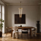Facing a dark framed artwork and a wooden dining table, this Clérachic pendant glows on its brass rod in a muted grey room.