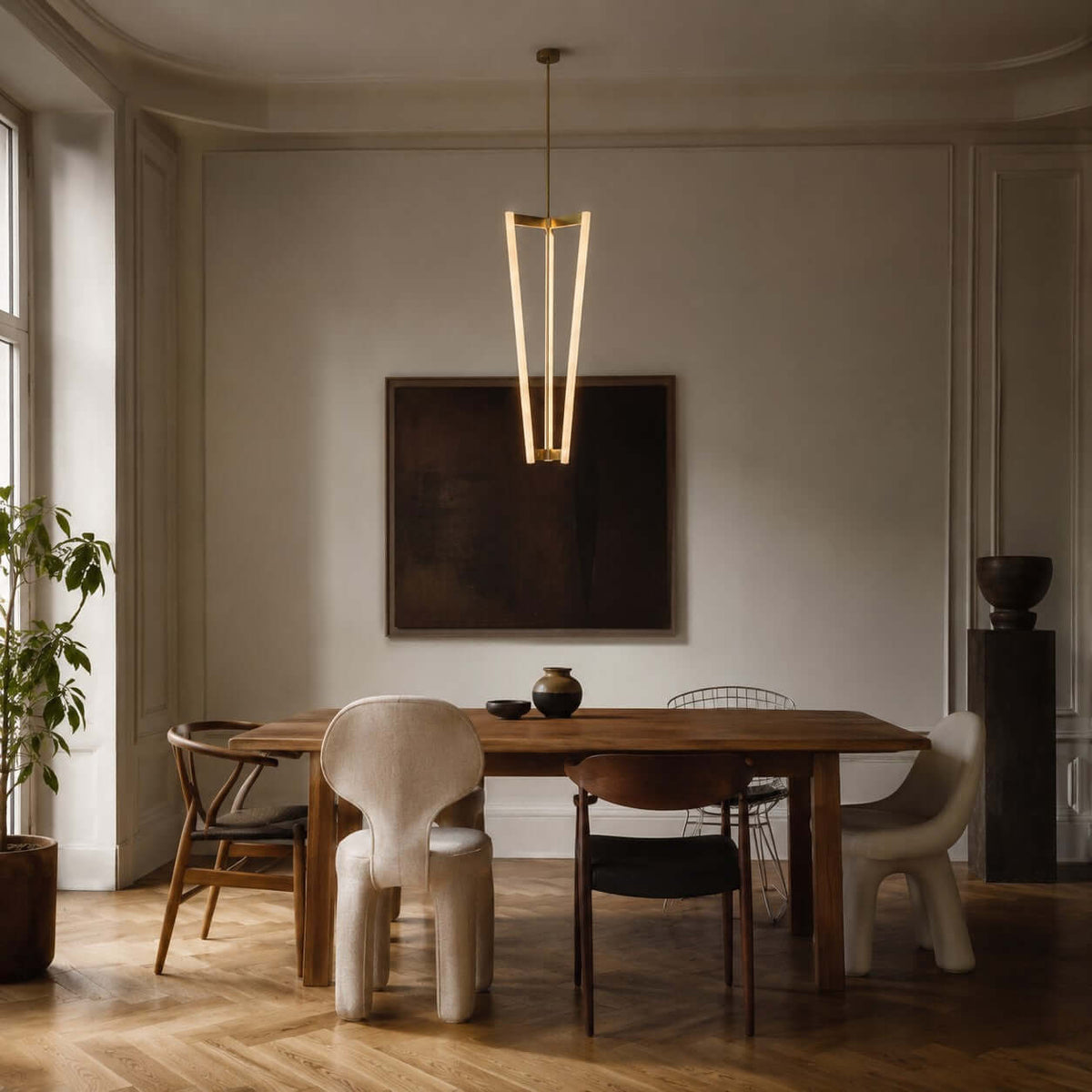 Facing a dark framed artwork and a wooden dining table, this Clérachic pendant glows on its brass rod in a muted grey room.