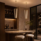 Two Clérachic pendants glow above a home bar with a marble counter and two stools, in a dim room lined with bottles.