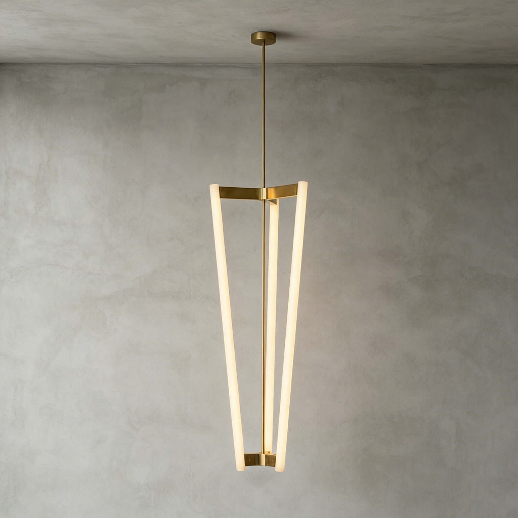 Against a grey plaster wall, this Clérachic pendant hangs from a ceiling canopy and brass rod, three slim LED tubes lit.