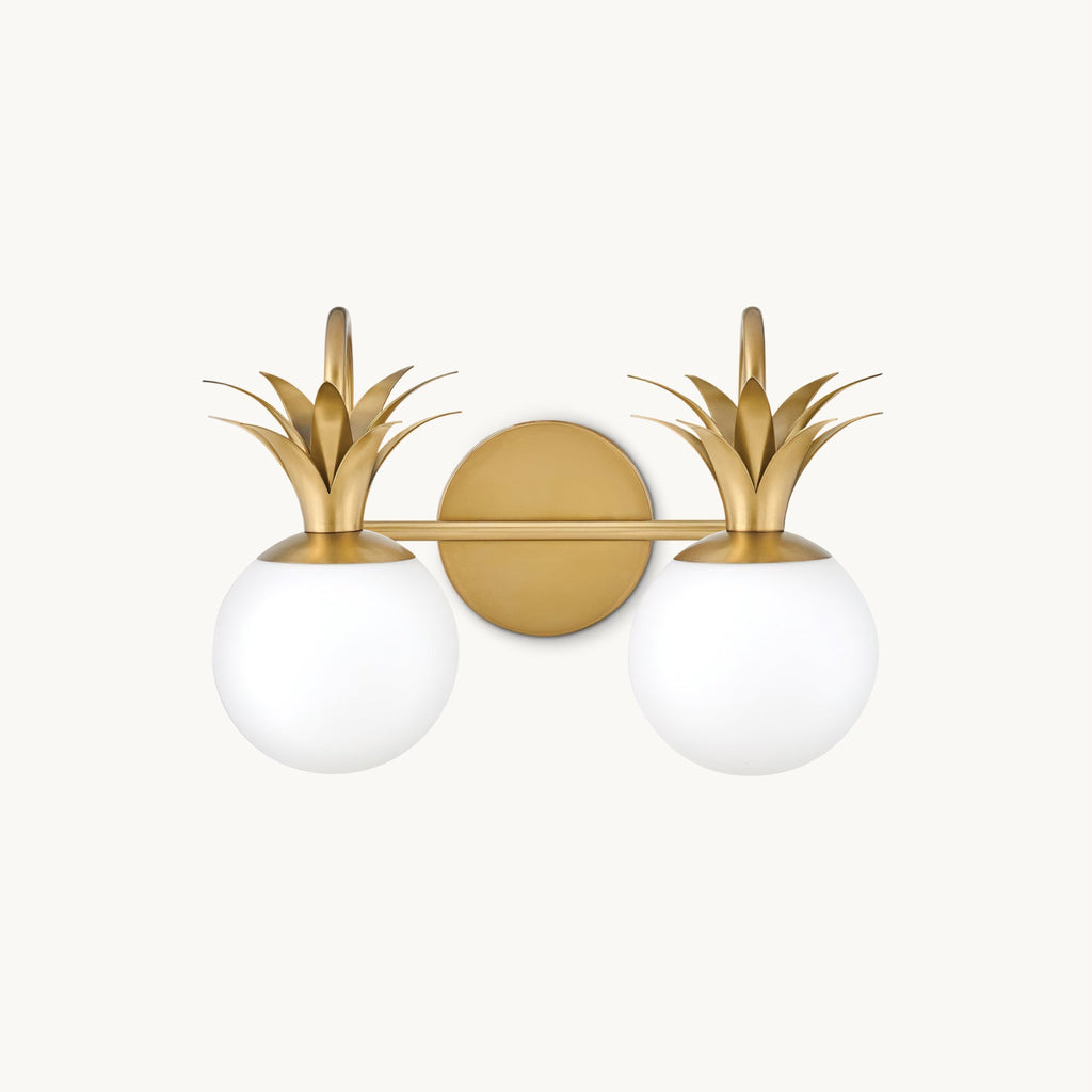 A two-light Clérachic wall light on a plain white backdrop, with opal glass globes under brass pineapple-leaf crowns on a round backplate.