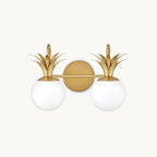 A two-light Clérachic wall light on a plain white backdrop, with opal glass globes under brass pineapple-leaf crowns on a round backplate.