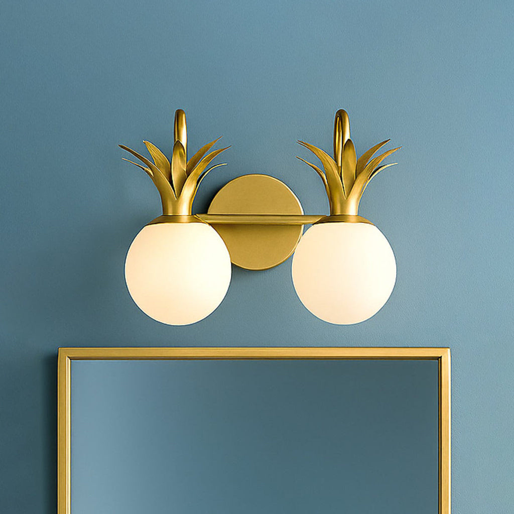 Two-light Clérachic wall light in brass with opal glass globes, mounted on a blue wall above a gold-framed mirror.