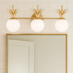 A three-light Clérachic wall light over a gold-framed mirror, with opal globes and brass leaf crowns against white tiles.