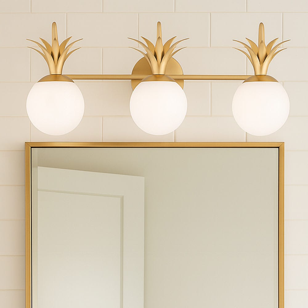 A three-light Clérachic wall light over a gold-framed mirror, with opal globes and brass leaf crowns against white tiles.