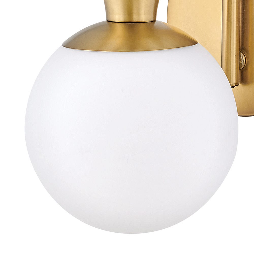 Close view of an opal white glass globe on this Clérachic wall light, with a brass cap and the brass backplate behind it.