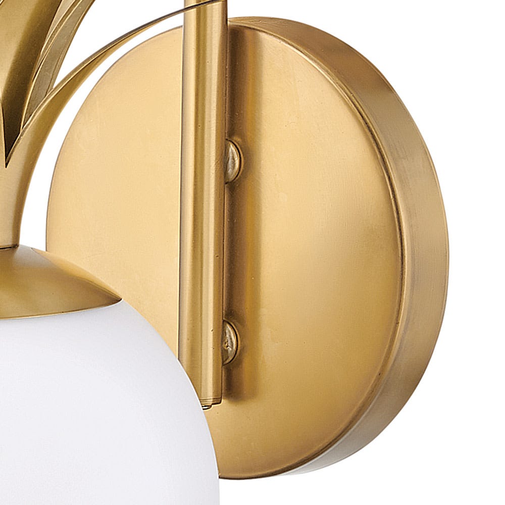 Close view of the round brass backplate and mounting bar of this Clérachic wall light, beside the edge of an opal globe.