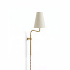Brass Clérachic plug-in wall light with a curved arm and a tapered white fabric shade, hung on a plain white wall.