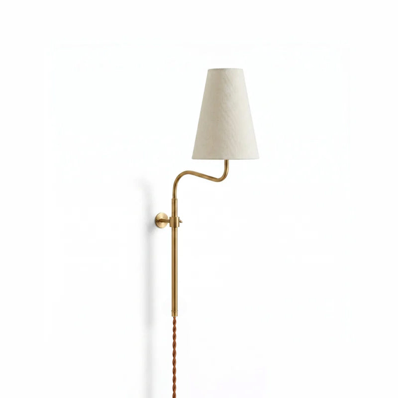 Brass Clérachic plug-in wall light with a curved arm and a tapered white fabric shade, hung on a plain white wall.
