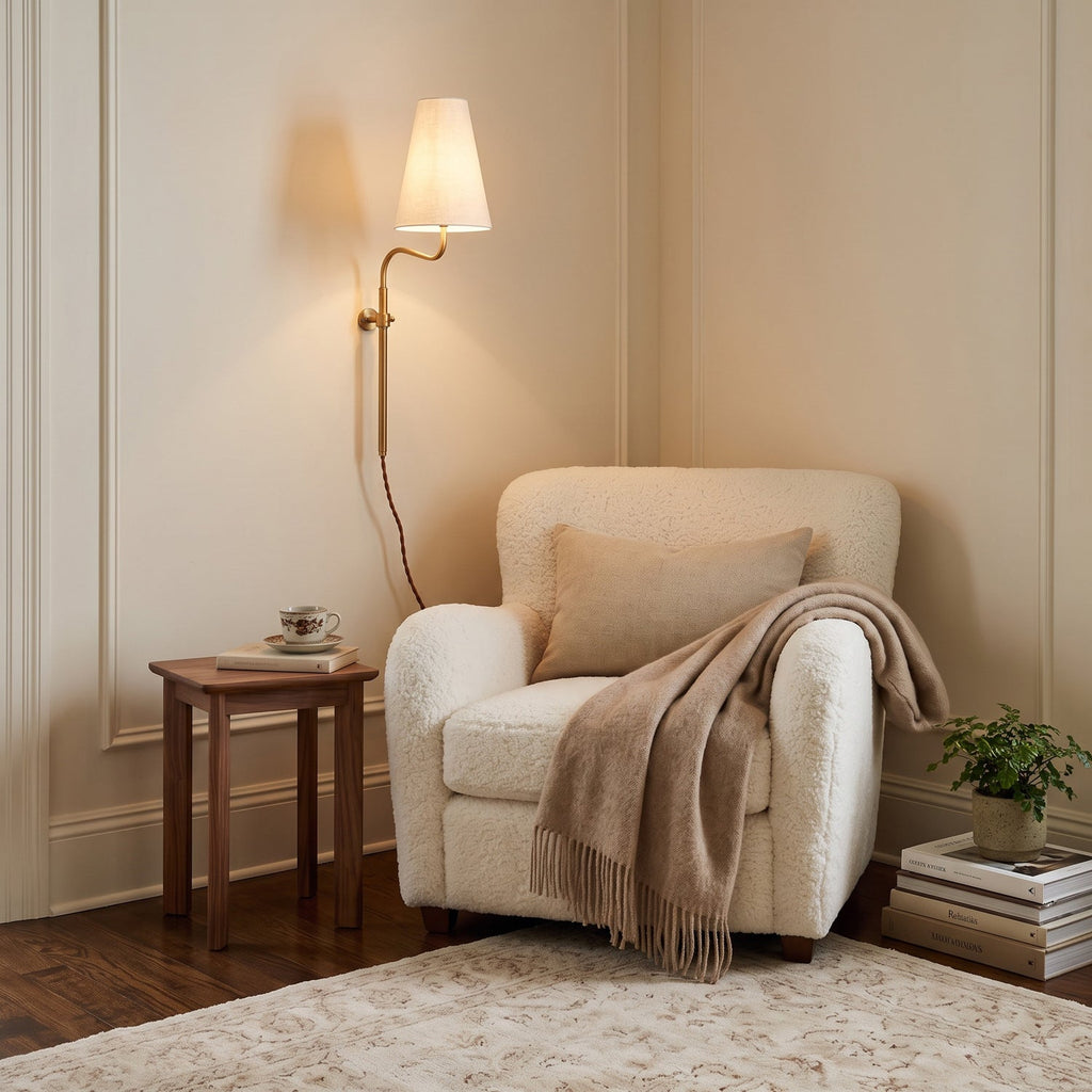 In a cream-panelled corner, this Clérachic brass wall light with a white shade glows above a boucle armchair and a small table.