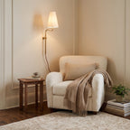 In a cream-panelled corner, this Clérachic brass wall light with a white shade glows above a boucle armchair and a small table.
