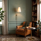 Above a tan leather armchair and a round brass side table, a Clérachic wall light glows against a sage-green panelled wall.
