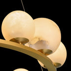 Close-up of the Clérachic chandelier's alabaster globes against black, one showing the raw cut edge and grey veining of the quarried stone.