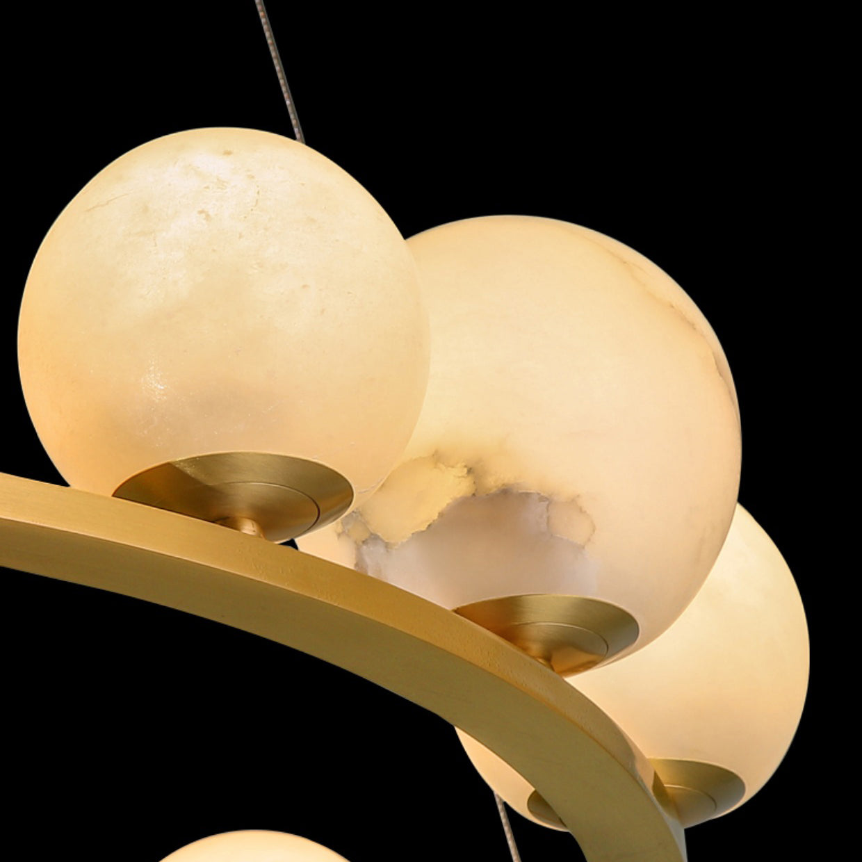 Close-up of the Clérachic chandelier's alabaster globes against black, one showing the raw cut edge and grey veining of the quarried stone.