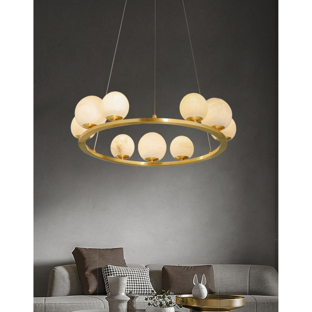 The Clérachic ring chandelier lit above a grey sofa on a dark wall, the alabaster globes reading as a slow cluster of moons.