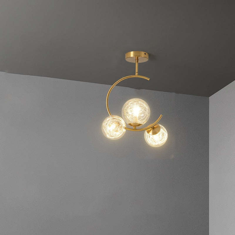 The Clérachic brass ring globe pendant in clear glass, its three lit globes curving over a grey corner ceiling and wall.