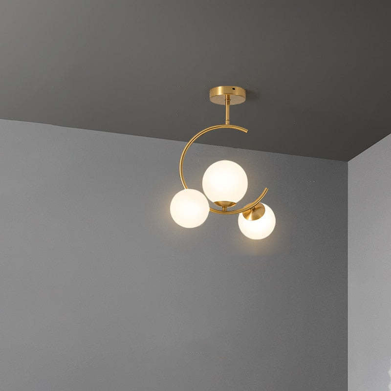 The Clérachic brass ring globe pendant in milky white glass, three softly lit spheres mounted close to a grey ceiling corner.