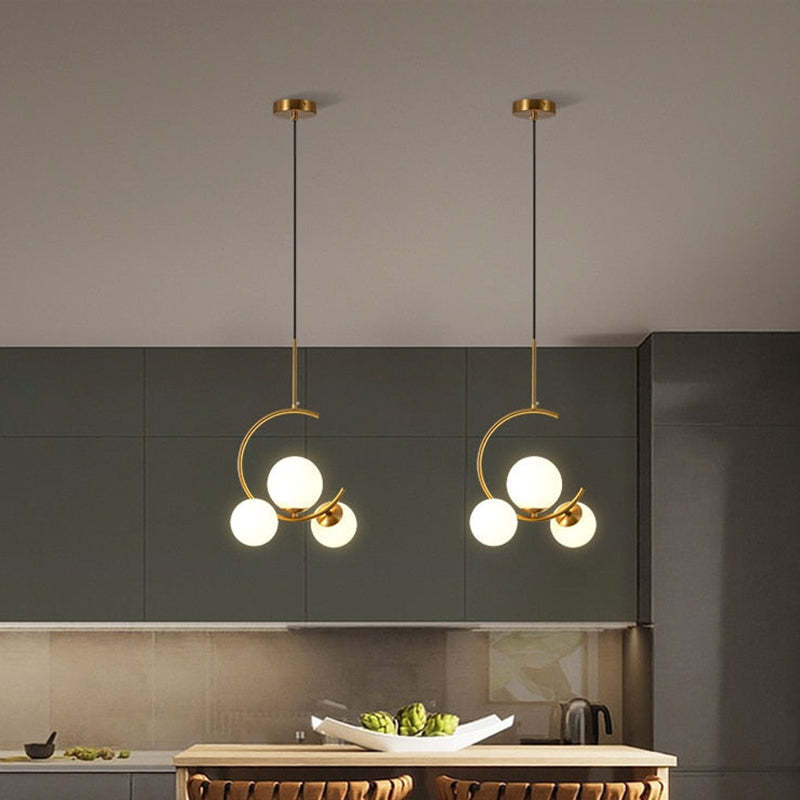 Two Clérachic brass ring globe pendants in milky white glass hung side by side above a kitchen island with dark green cabinetry.
