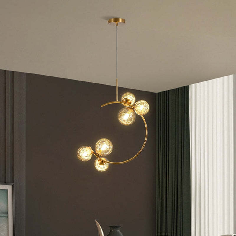 The Clérachic brass ring globe pendant in clear glass, six lit globes over a living room console with dark curtains and a vase.
