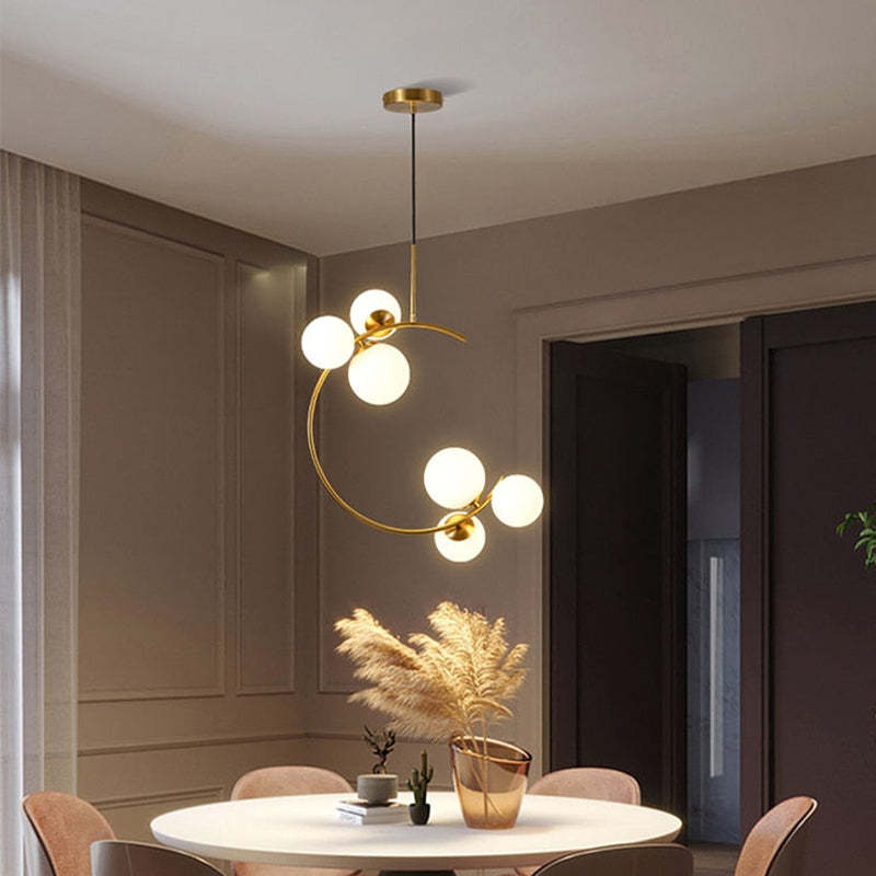 The Clérachic brass ring globe pendant in milky white glass lit above a round dining table set with pampas grass and pink chairs.
